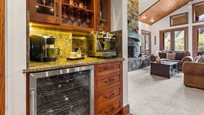 A kitchen with a built-in oven, a coffee maker, and a wine cooler. There is a stone wall and a wooden ceiling.