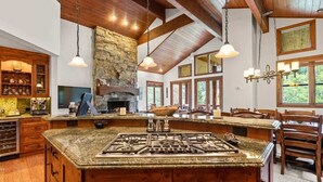 A spacious kitchen with a large island, wooden cabinets, and a stone fireplace.