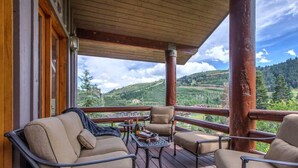 A wooden deck with outdoor furniture, a table, and a scenic view of hills and trees.