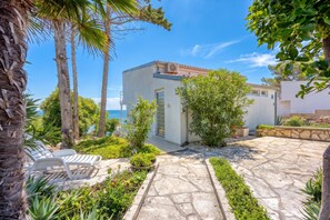A coastal property with a stone patio, a white building with a tiled roof, and a view of the sea.