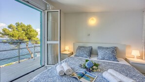 A hotel room with a bed, two bedside lamps, a window with a view of the sea, and a balcony.