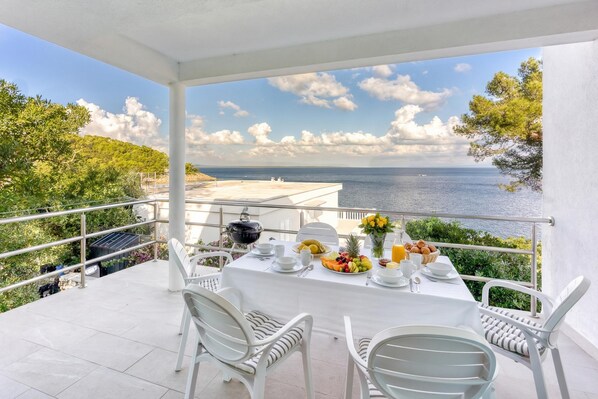 Un balcon avec une table préparée pour le petit-déjeuner, donnant sur une étendue d’eau et une végétation luxuriante.