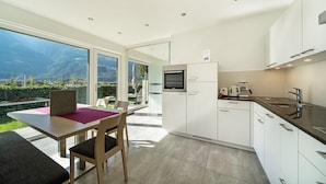 A modern kitchen with a large window, a dining area with a table and chairs, and a view of the mountains. - Apartment "Weinreichhof Marie & Max" with Mountain View, Private Terrace & Wi-Fi (Ciardes)