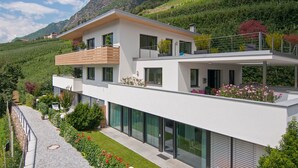 A modern two-story house with a balcony, large windows, and a garden. - Apartment "Weinreichhof Marie & Max" with Mountain View, Private Terrace & Wi-Fi (Ciardes)