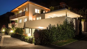 A modern two-story house with a balcony, large windows, and a well-lit entrance. - Apartment "Weinreichhof Marie & Max" with Mountain View, Private Terrace & Wi-Fi (Ciardes)