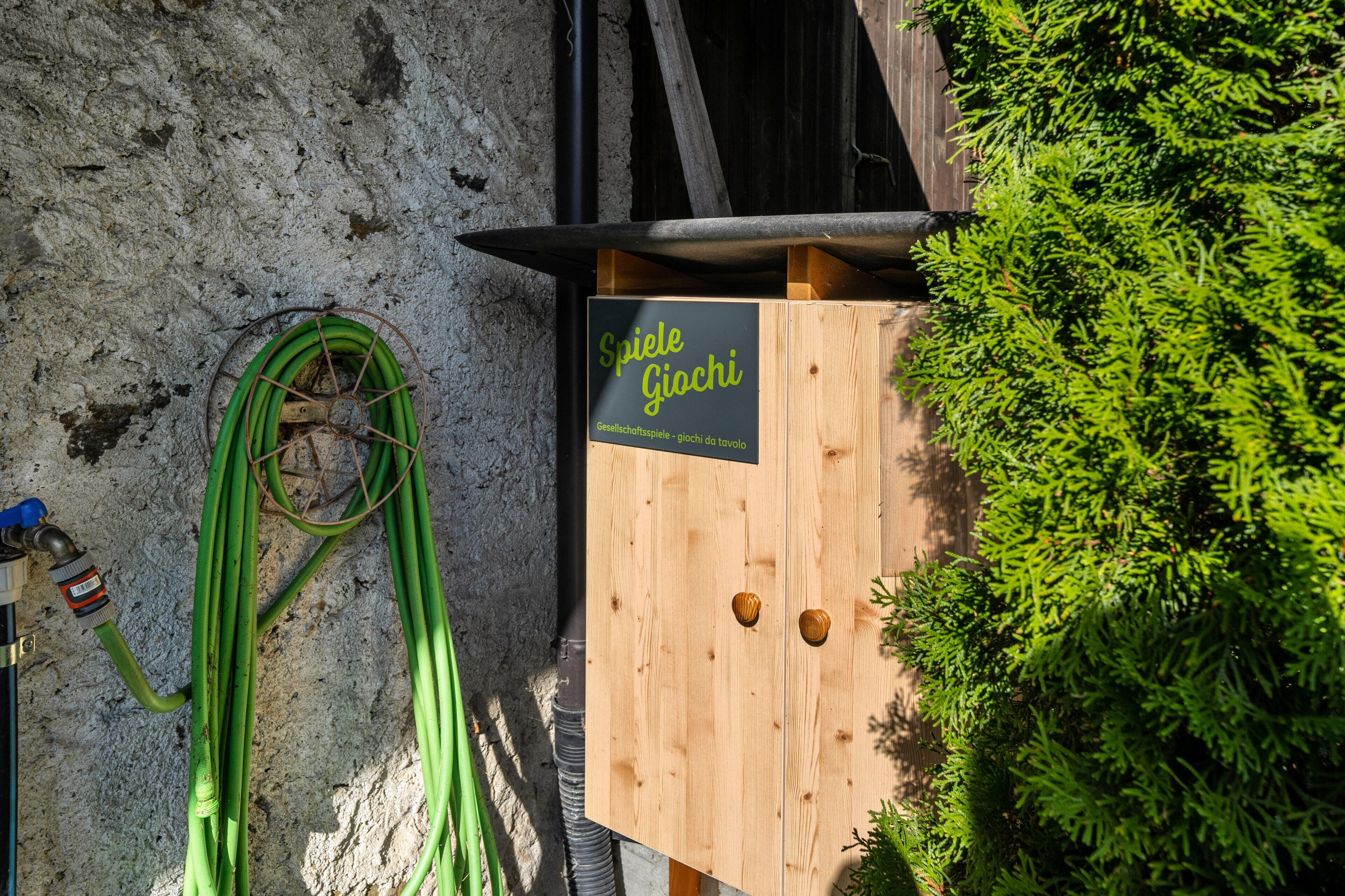 Une structure en bois, sur laquelle est apposée une enseigne indiquant « Spiele Giochi », est adossée à un mur à texture.