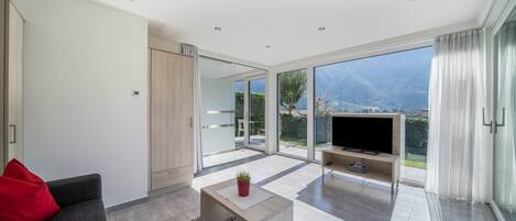 Ein modernes Wohnzimmer mit einer Couch, einem Couchtisch, einem Fernseher und einer Schiebetür zu einem Balkon mit Bergblick.