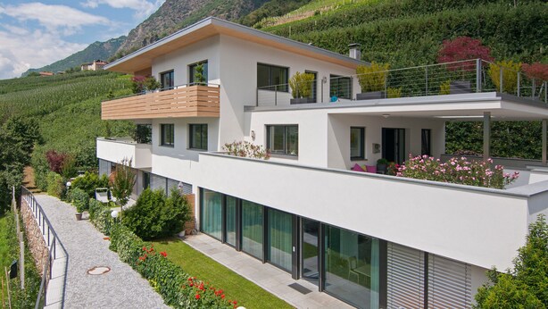 Una casa moderna de dos pisos con balcón, ventanas grandes y un jardín.