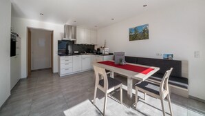 Una cocina moderna con armarios blancos, una mesa de comedor con camino de mesa rojo y un sofá gris.
