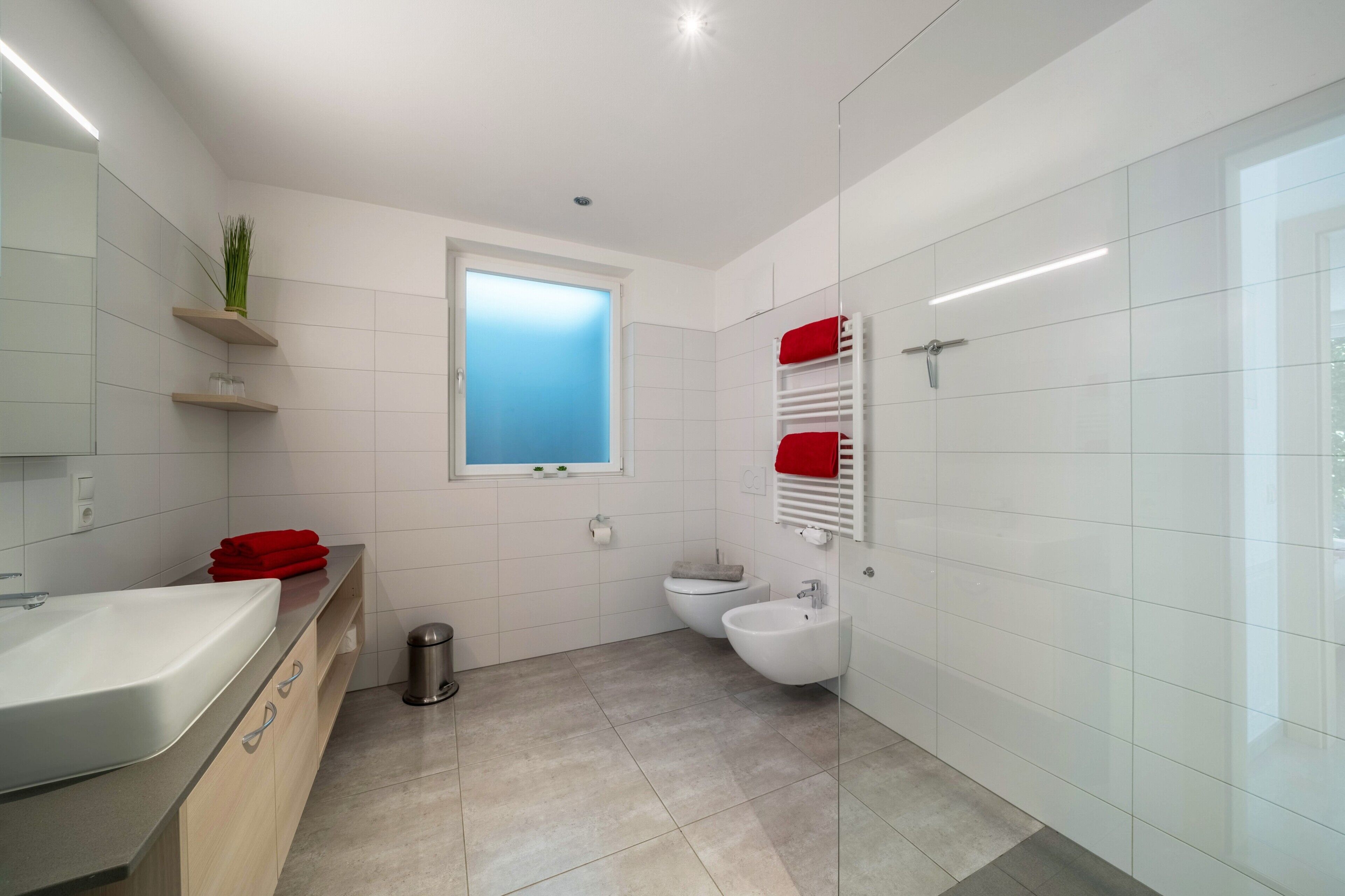Ein modernes Badezimmer mit Waschbecken, Toilette, Bidet und Spiegel.