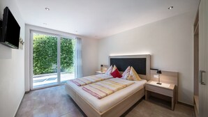 Un dormitorio moderno con una cama grande, una mesita de noche, un televisor montado en la pared y un ventanal corredero que da a un balcón.