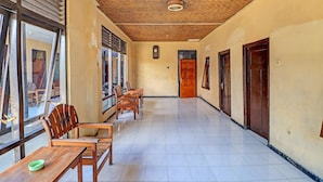 A corridor with wooden chairs and tables, a tiled floor, and a ceiling with a woven pattern. - SPOT ON 92028 Hotel Surya Near Pelabuhan Gilimanuk (Melaya)