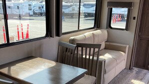 Een compact camperinterieur met een eethoek, een comfortabele zithoek en grote ramen met uitzicht op de omgeving.