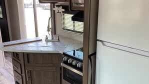 Een kleine keuken met houten keukenkastjes, een inbouwoven, een magnetron en een witte koelkast.