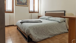 Una camera da letto con un letto, una testata in legno, una finestra con tende, un termosifone e un quadro appeso al muro.