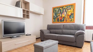 Un soggiorno moderno con un divano grigio, una TV a schermo piatto, un mobile contenitore in legno e un quadro astratto colorato appeso al muro.