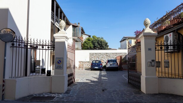 Un cancello chiuso con due auto parcheggiate all'interno, un vialetto in pietra e un cielo azzurro intenso.