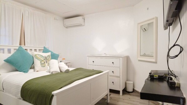 Un dormitorio blanco con cama, cómoda, espejo y equipo de aire acondicionado.