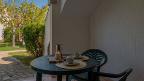 Une table ronde avec deux chaises, une bougie et deux tasses, sur une terrasse donnant sur un jardin et un bâtiment.