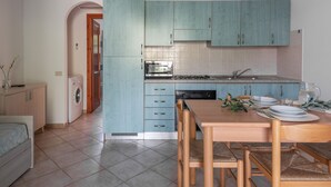 Une cuisine compacte avec des meubles de couleur turquoise, un four à micro-ondes, une cuisinière et un coin repas comprenant une table et des chaises.