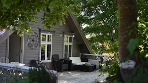 A cozy outdoor seating area with a sofa, chairs, and a table, surrounded by greenery and a tree.