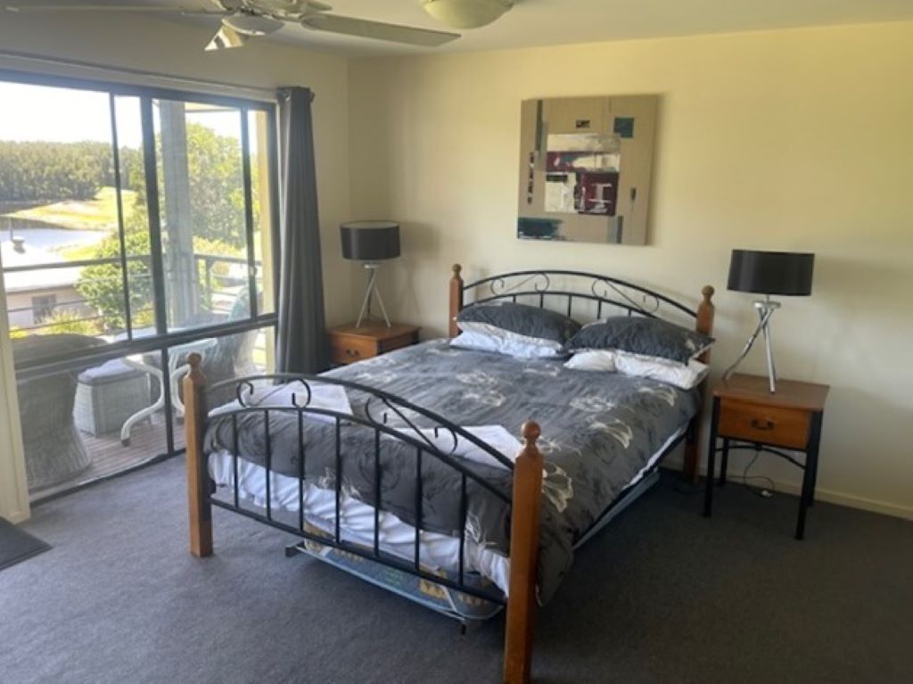 Quarto com estrutura de cama de metal, uma janela grande com vista para um lago e duas mesas de cabeceira com luminárias.