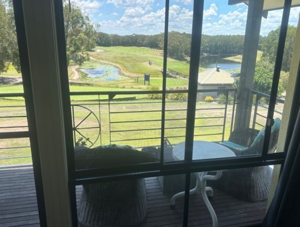 Vista desde una habitación con un amplio ventanal que da a un campo de golf, incluyendo un estanque y un edificio.
