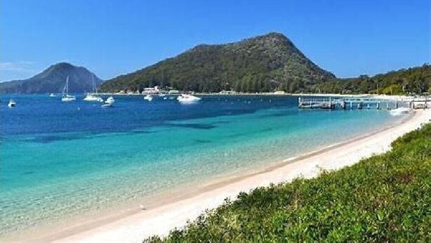 Ein Strand mit klarem türkisblauem Wasser, Booten und einem Berg im Hintergrund.
