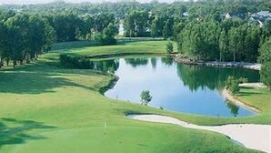 Ein Golfplatz mit Teich, Sandbunkern und umliegenden Bäumen.