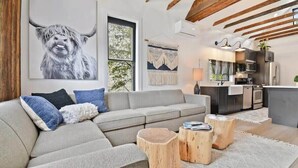 A modern living room with a grey sofa, wooden stools, and a large window.