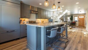 A modern kitchen with a central island, bar stools, and pendant lighting.