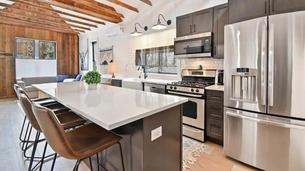 A modern kitchen with a central island, stainless steel appliances, and exposed wooden beams.
