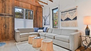 A modern living room with a grey sectional sofa, wooden stools, and a large window.