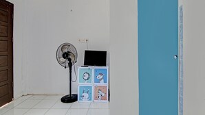 Een kamer met een betegelde vloer, een houten deur, een blauwe deur, een ventilator en een klein tafeltje met een laptop en een decoratief object.