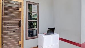 Een kamer met een houten deur, een raam met een metalen traliewerk en een witte kast met een laptop erop.