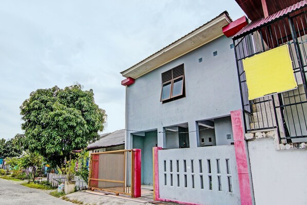 A two-story building with a gated entrance, a large tree in front, and a yellow sign on the right side.