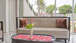 Uma sala de estar moderna com sofá, mesa de centro com um vaso de flores e vista para uma escada e palmeiras lá fora.