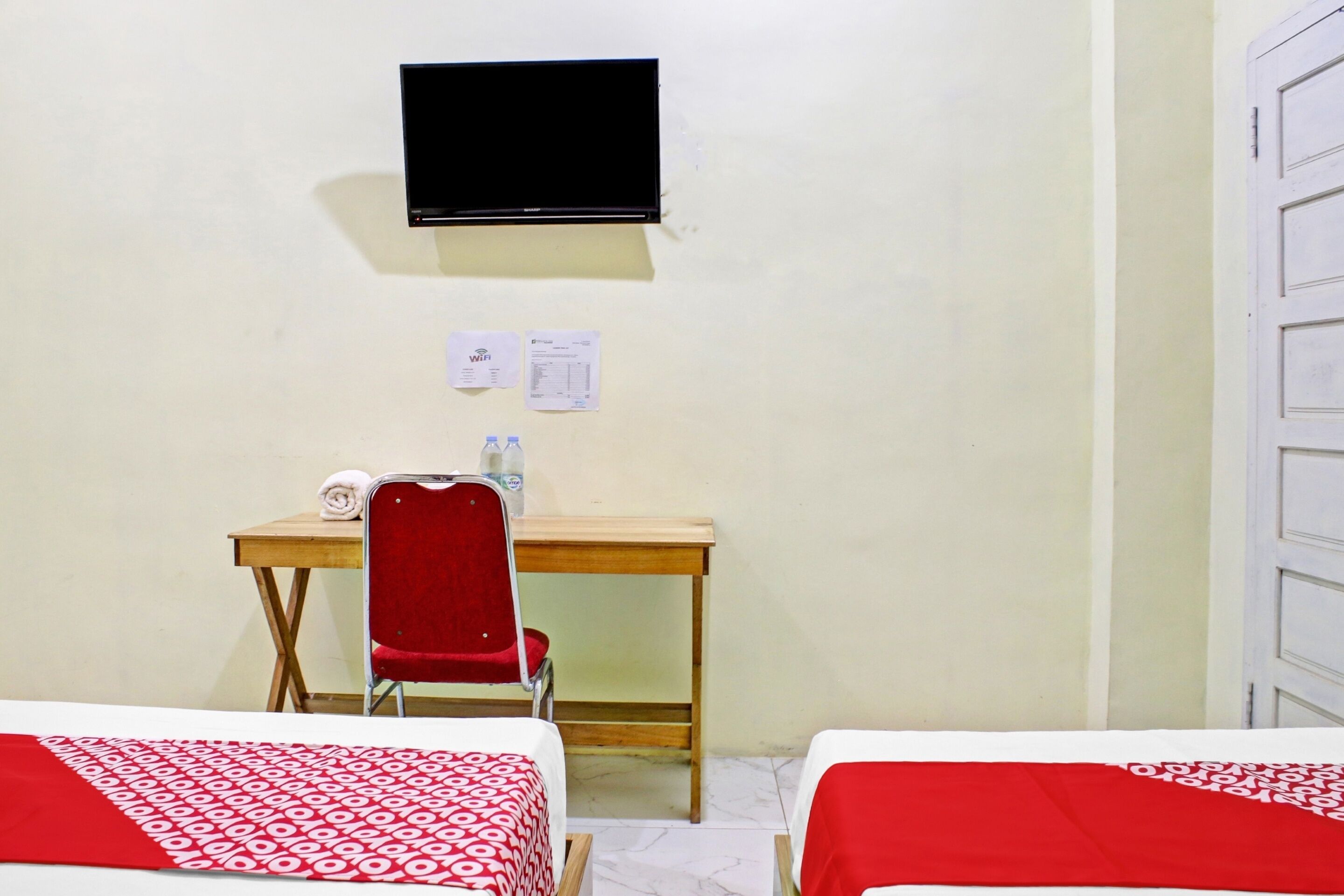 A hotel room with two beds, a desk, a chair, a television, and a door.