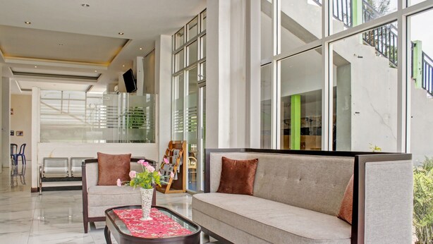 Um lobby moderno com um sofá, uma mesa de centro com um vaso de flores e uma escadaria com guarda-corpo de vidro.