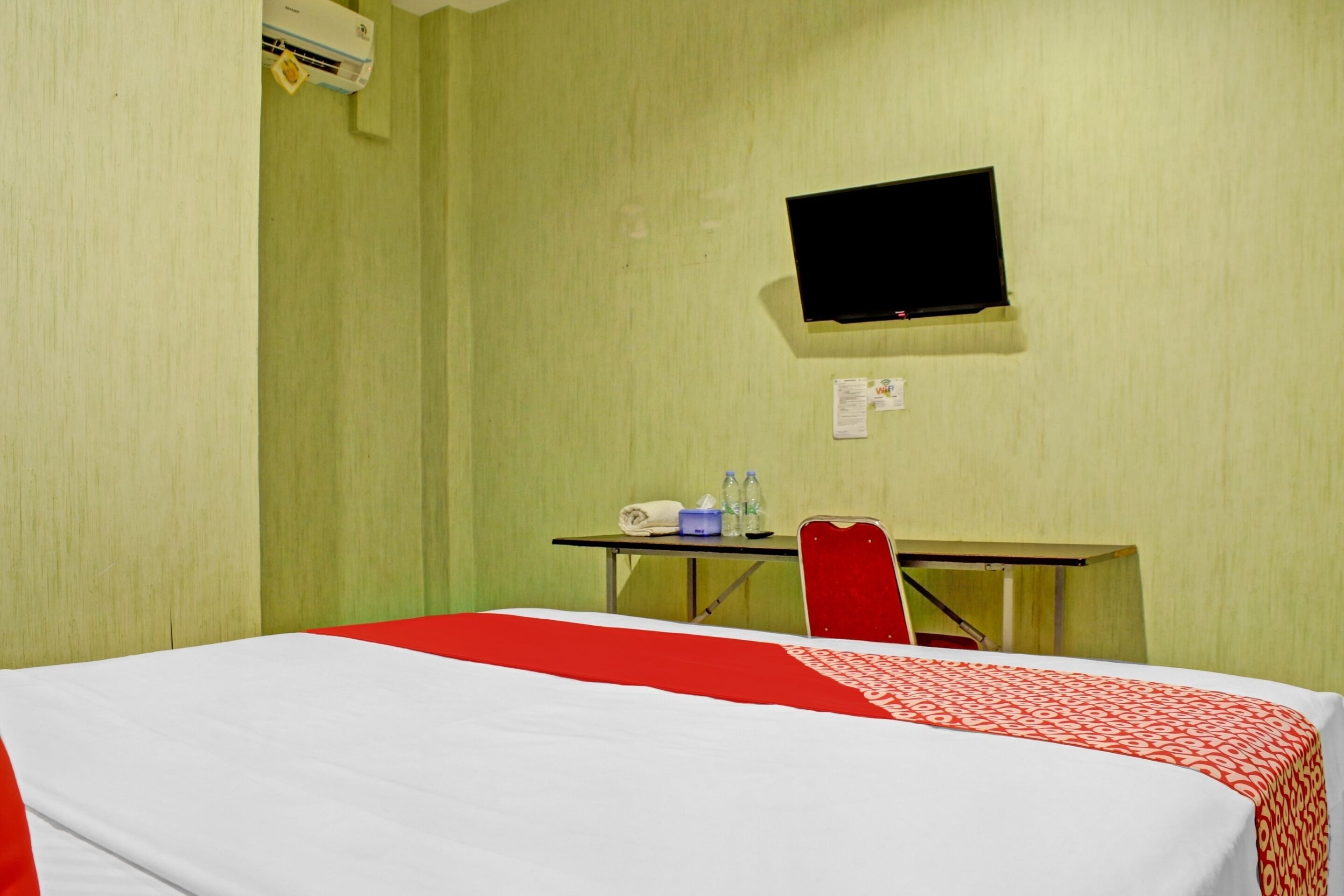 A hotel room with a bed, a desk, a chair, a flat-screen TV, and a window.