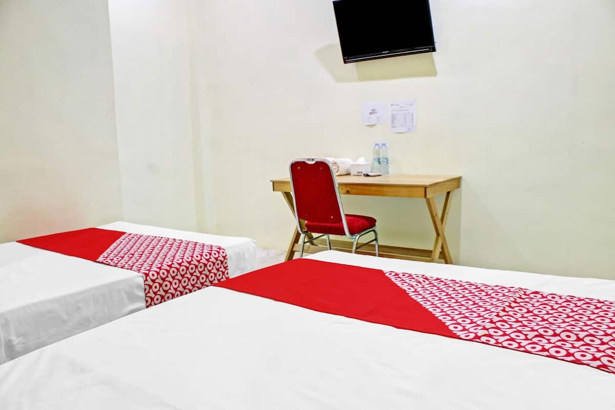 Ein Hotelzimmer mit zwei Einzelbetten, einem Schreibtisch, einem Stuhl, einem Fernseher und einer Wasserflasche auf dem Schreibtisch.