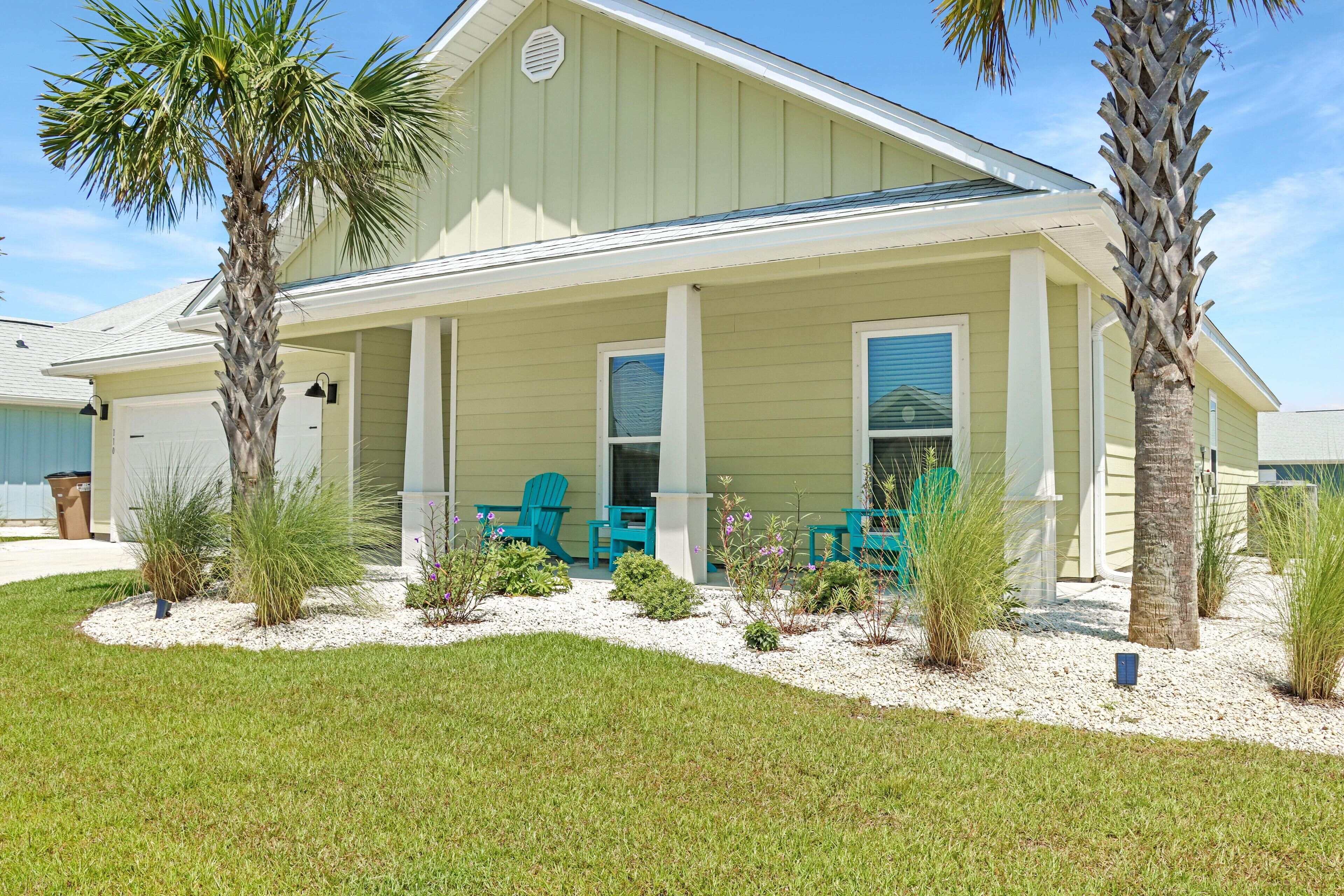 A house with a covered porch, palm trees, and outdoor seating.