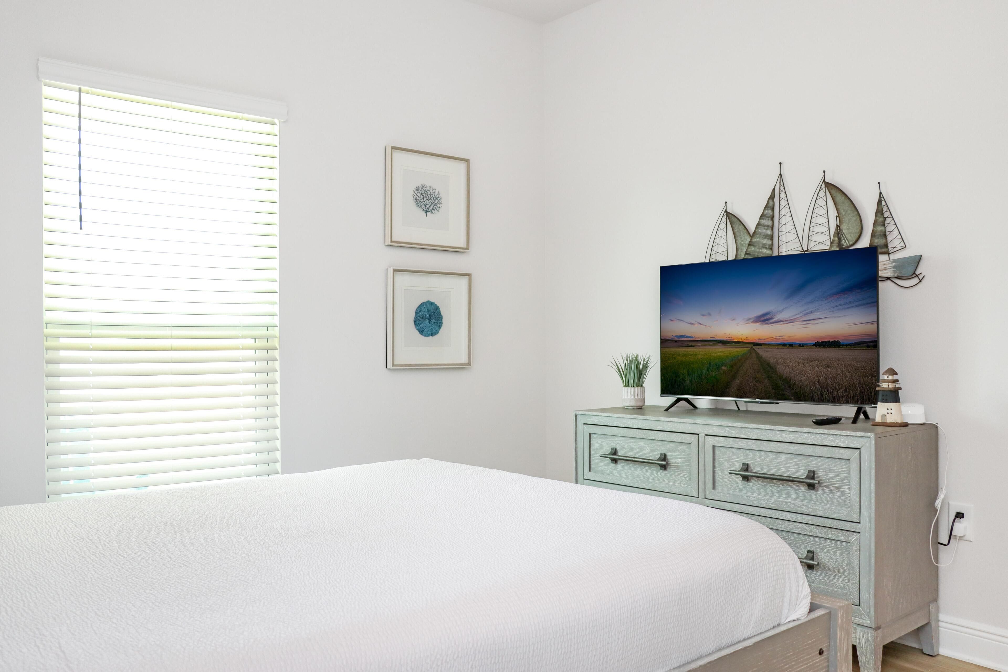 Une chambre à coucher comprenant un lit, une commode, un téléviseur et deux tableaux encadrés accrochés au mur.