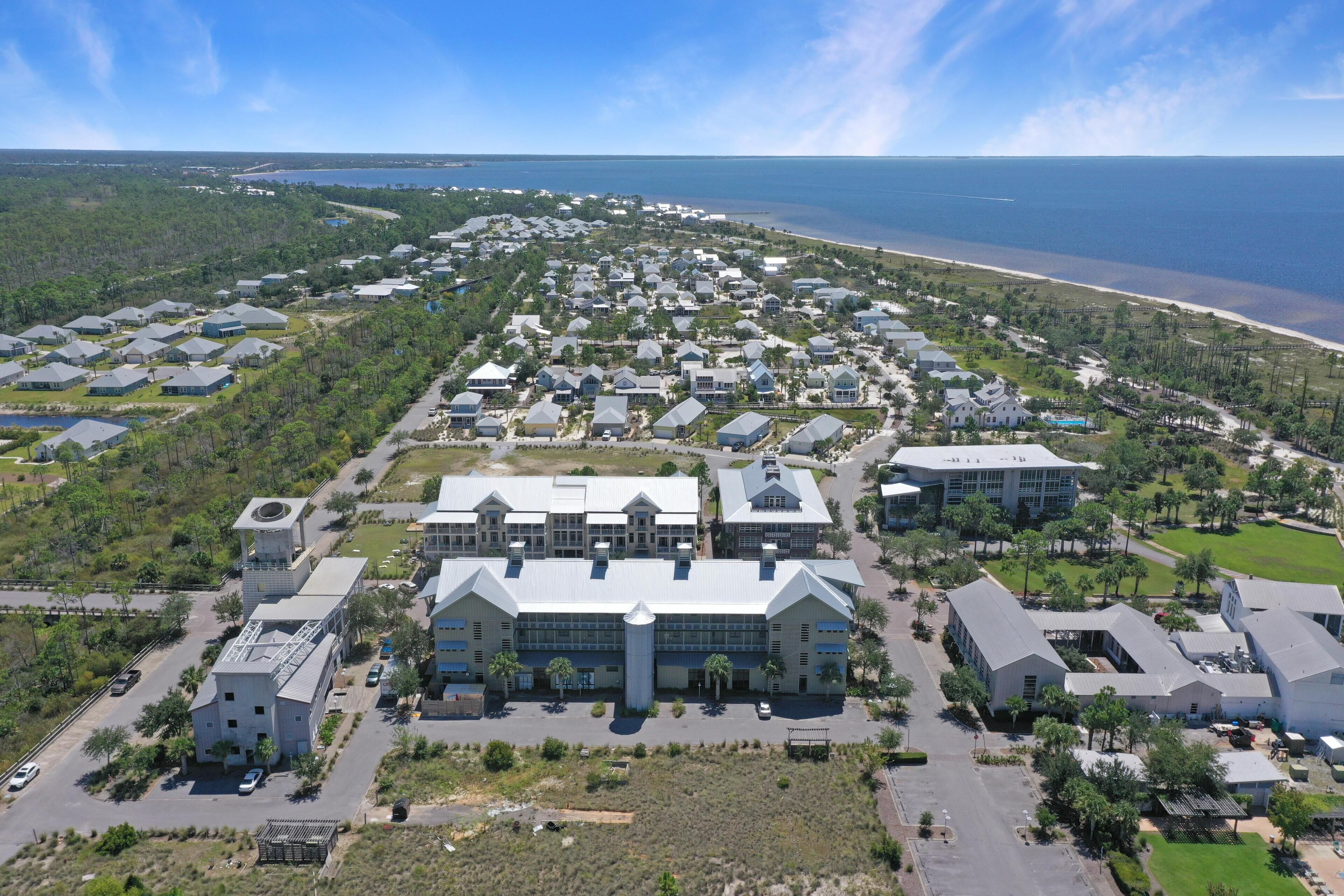 An aerial view of a residential area with multiple houses, a large central building, and a beach in the background.