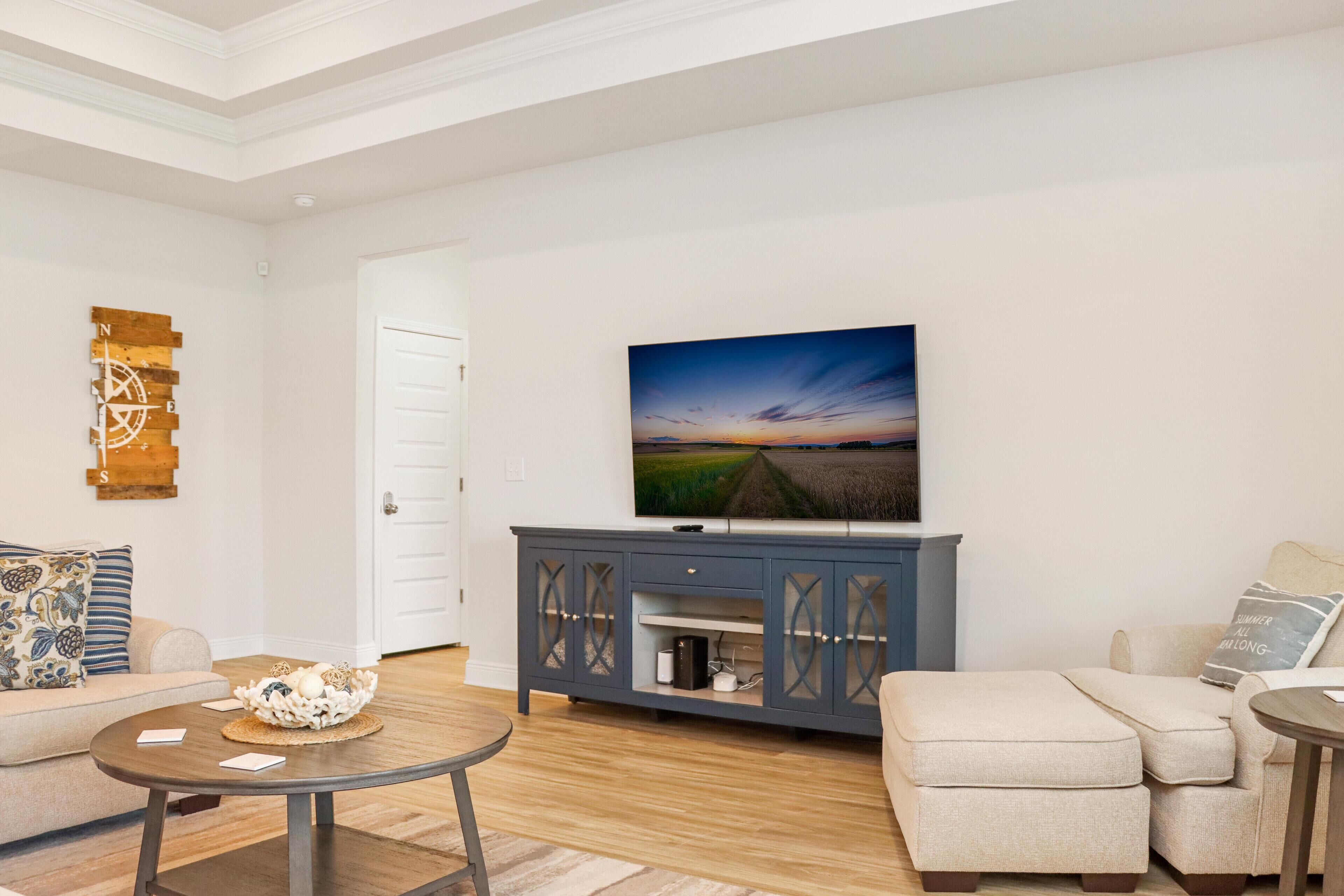 Una sala de estar con una televisión de pantalla plana montada en la pared, un aparador de madera con puertas de cristal, un sofá beige y una mesa de centro redonda.