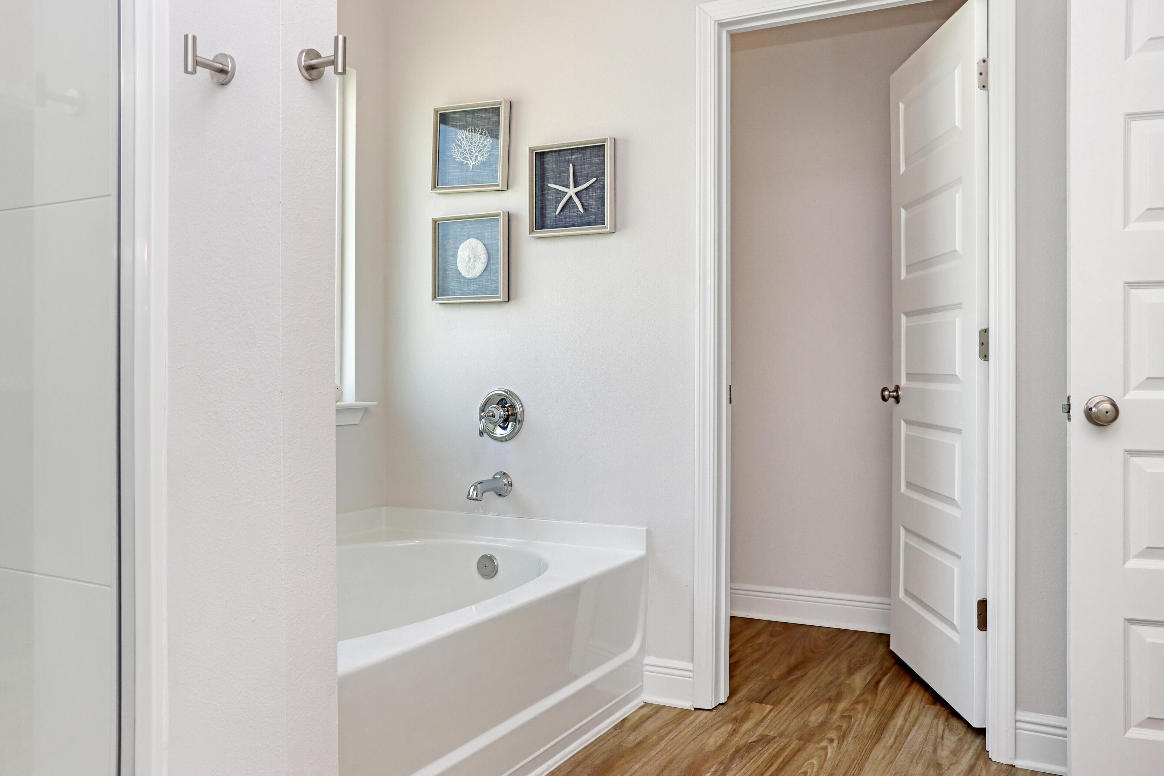 A bathroom with a bathtub, a shower, and a door leading to another room.