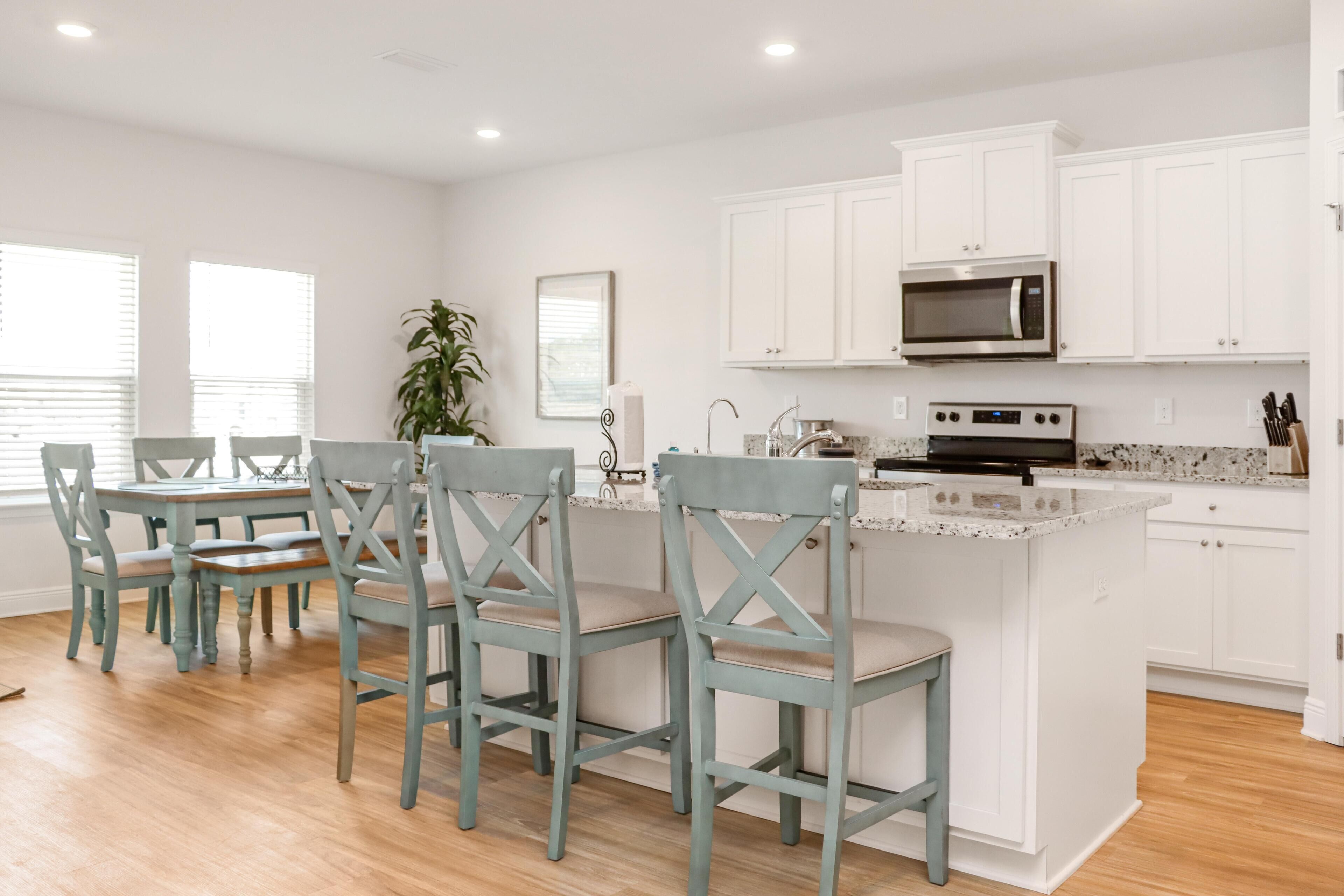 A modern kitchen with white cabinets, a central island, and a dining area with chairs.
