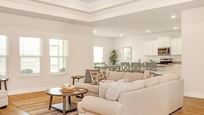 A spacious living room with a beige sectional sofa, a coffee table, and a dining area in the background. - Beach Haven at WindMark (Port St. Joe)