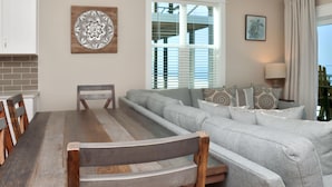 A living room with a wooden dining table, grey sofa, and a large window with blinds. - The Great White 1 (Port St. Joe)