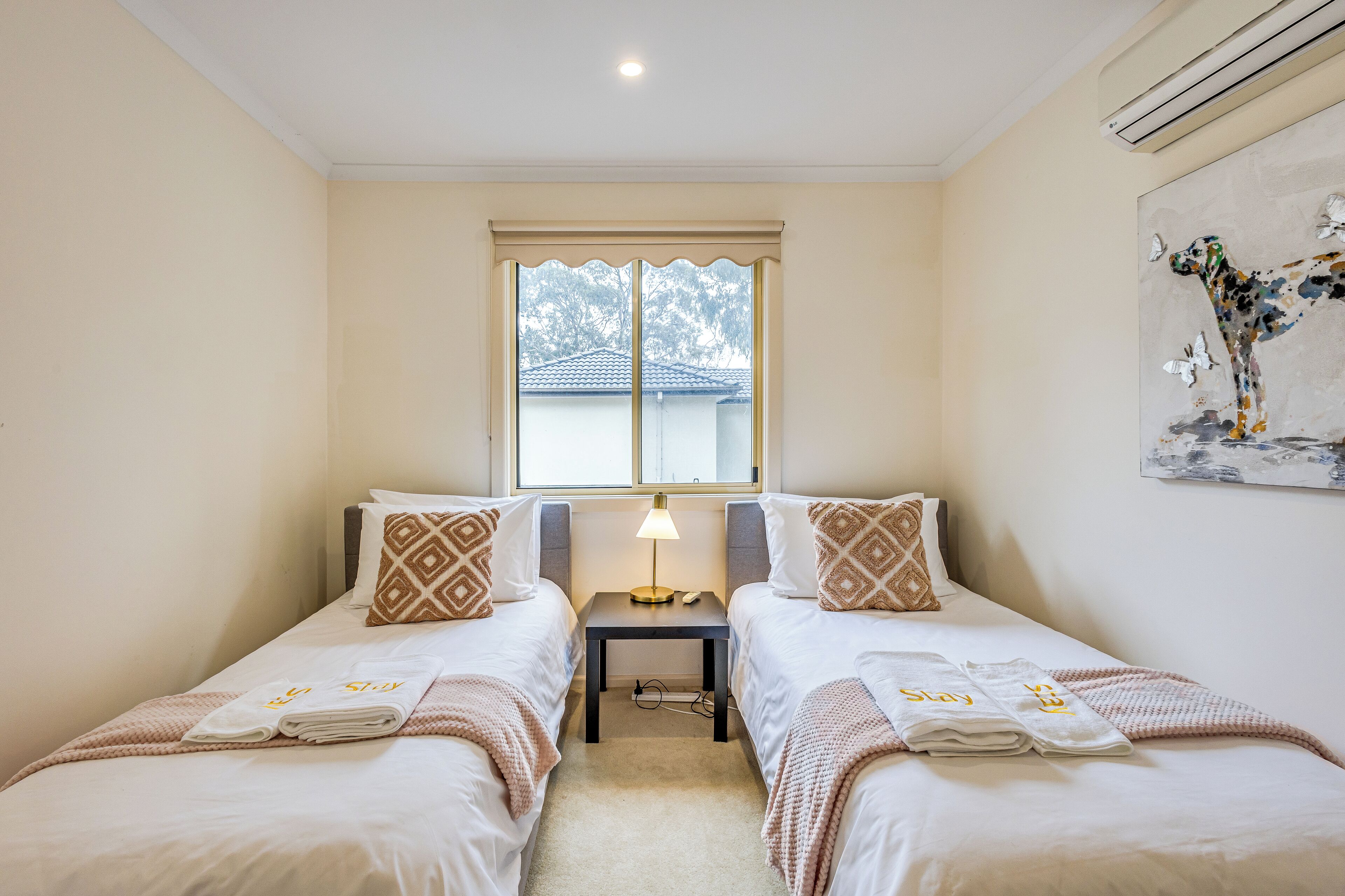 A twin room with two beds, a nightstand, a lamp, and a window with a view of a building.
